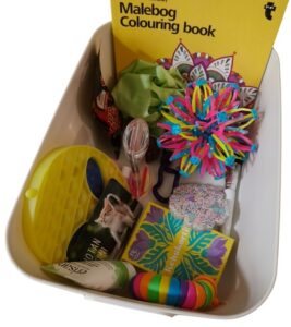 Laatikossa widget-leluja, käsirasvaa, värityskirja ja korttipakka.